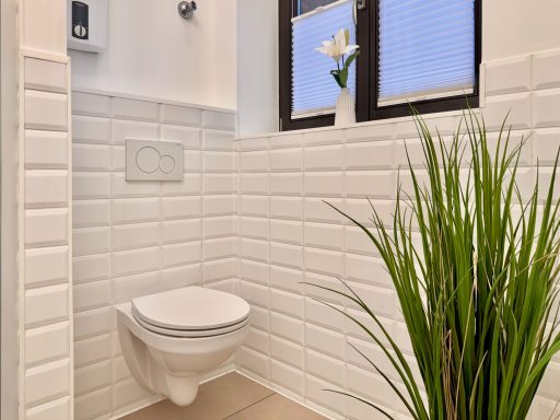 Helles Badezimmer mit weißem WC, großen Fliesen und einer Pflanze in der Ecke.