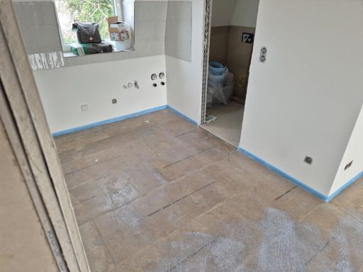 Leerer Raum mit blauer Abkleberlinie und unvollständig verlegtem Boden.