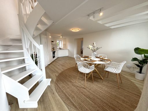 Heller Wohnraum mit Treppe, Esstisch und modernen Stühlen auf einem runden Teppich.