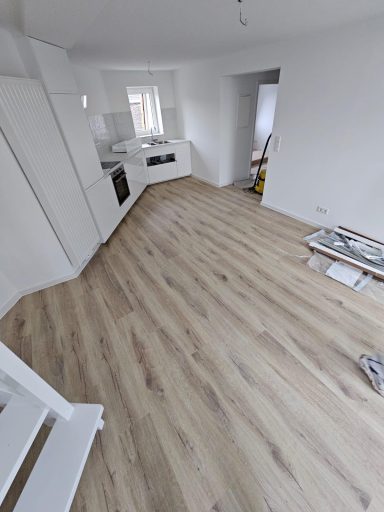 Heller, leerer Raum mit Holzfußboden und moderner Küche im Hintergrund.