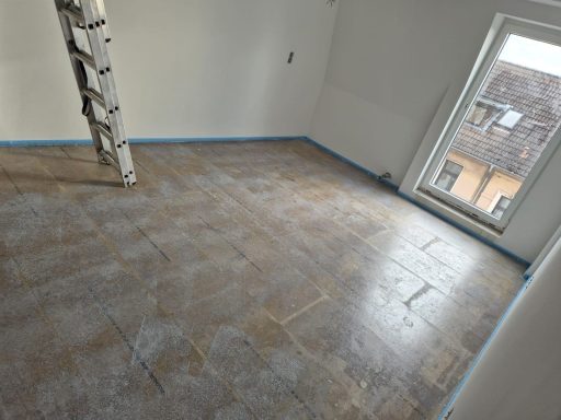 Leere, unmöblierte Zimmer mit gefliester Boden und Fenstern. Leiter im Hintergrund.