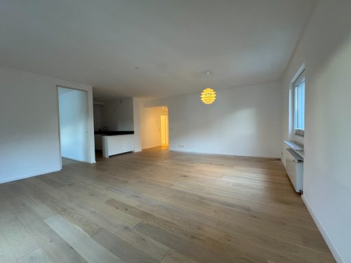 Heller, leerer Raum mit Holzfußboden und großen Fenstern.