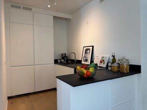 Moderne Küchenzeile mit schwarzer Arbeitsplatte, Obstkorb und dekorativen Elementen.