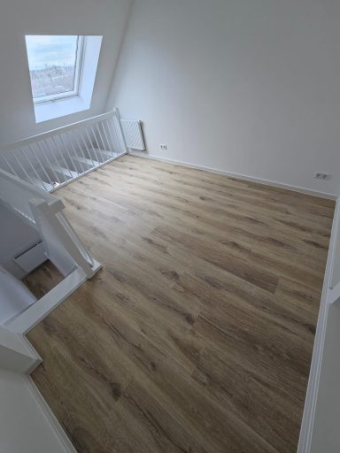 Helle, leere Wohnung mit Sicht auf Treppe und Holzboden.