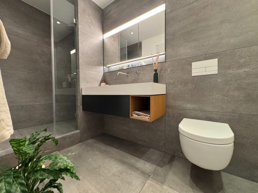 Modernes Badezimmer mit wandmontiertem Waschbecken, Dusche und Pflanzen.