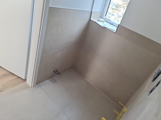 Leerer Raum mit beige Wandverkleidung und Fenster, unvollendeter Bodenbereich.