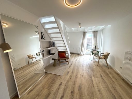 Heller, moderner Raum mit Treppe, großen Fenster und gemütlicher Sitzecke.