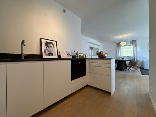 Moderne Küche mit weißen Möbeln, schwarzer Arbeitsfläche und Essbereich im Hintergrund.