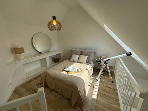Gemütliches Schlafzimmer mit Bett, Spiegel und einem Teleskop unter einer Dachschräge.