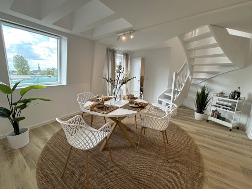 Heller Essbereich mit runder Teppich, weißen Stühlen und treppen in einem modernen Raum.