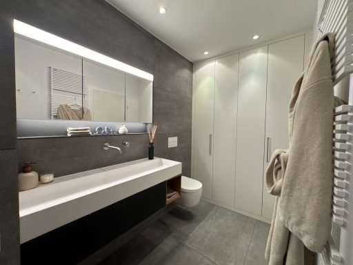 Modernes Badezimmer mit Waschbecken, WC und Spiegel über der Ablage. Helle Beleuchtung.
