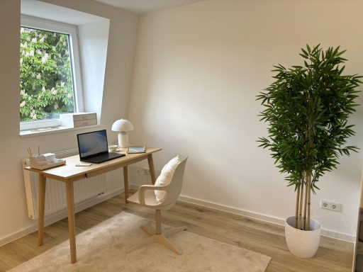 Heller Raum mit Schreibtisch, Stuhl, Laptop und einer Pflanze in einem Topf.