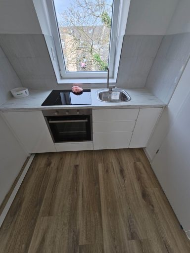 Moderne Küche mit Fenster, Spüle und Herd, Holzboden in hellen Farbtonen.