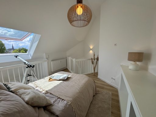 Helles Schlafzimmer mit Bett, Lampe und Fenstern, die einen Blick nach draußen bieten.