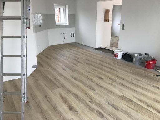 Heller Raum mit Laminatboden, Leiter und Malerutensilien im Hintergrund.