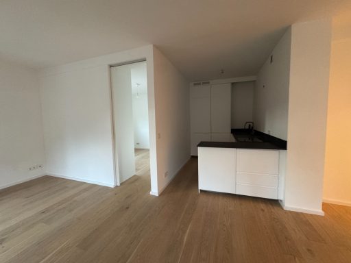 Helle, leere Wohnung mit offener Küche und Holzfußboden.