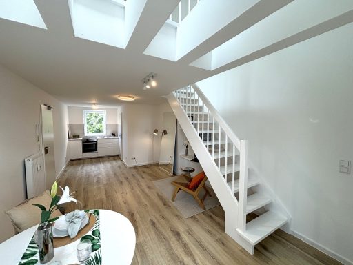 Helles, modernes Wohnzimmer mit Treppe und offener Küche im Hintergrund.