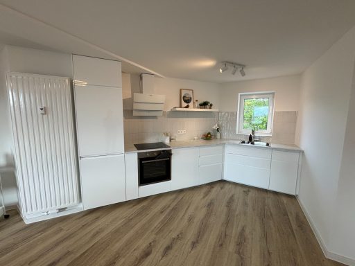 Moderne, helle Küche mit weißen Möbeln und Holzfußboden. Fenster mit Pflanzen.