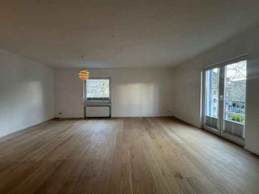 Heller, leerer Raum mit Holzfußboden und großen Fenstern.
