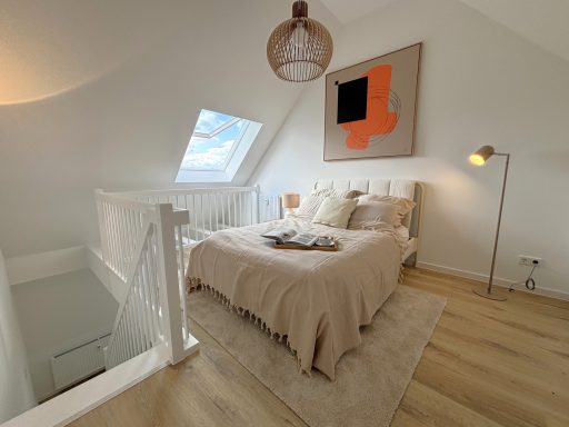 Helles Schlafzimmer mit Bett, Stehlampe und modernem Kunstwerk an der Wand.